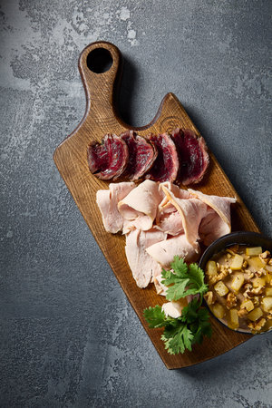Vertical top-down shot of a selectable meat assortment - roast beef, turkey pastrami, and chicken pÃ¢tÃ©, arranged on a wooden board against a modern gray concrete texture.の写真素材