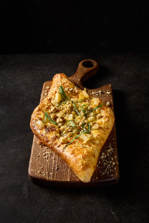 Vertical side perspective of a creatively crafted Adjarian khachapuri, adorned with pear, nuts, and cheese, set on a textured wooden board.の写真素材