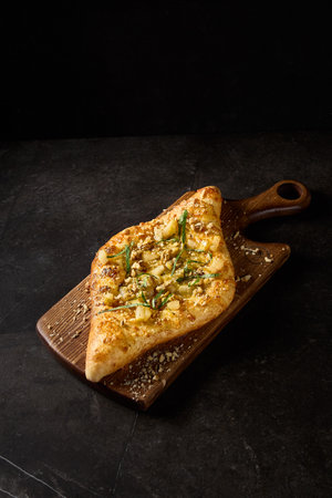 Vertical side perspective of a creatively crafted Adjarian khachapuri, adorned with pear, nuts, and cheese, set on a textured wooden board.の写真素材