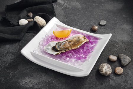 Fresh Imperial oyster served on crushed ice with a vibrant lemon wedge, a classic delicacy on a white plate.の写真素材