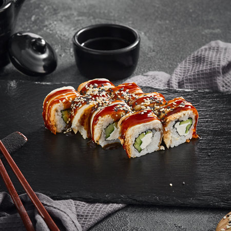A delectable Canada maki roll with succulent eel and rich unagi sauce, sprinkled with sesame seeds, presented on a black slate.の写真素材