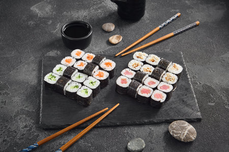 A classic assortment of hosomaki sushi featuring salmon, tuna, cucumber, and eel, beautifully arranged on a black slate with soy sauce.の写真素材