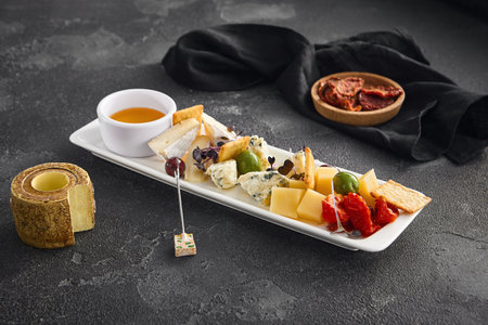 A curated selection of cheeses, sun-dried tomatoes, and olives, perfect for wine pairing, presented on a plate with minimalist style on a dark background.の写真素材