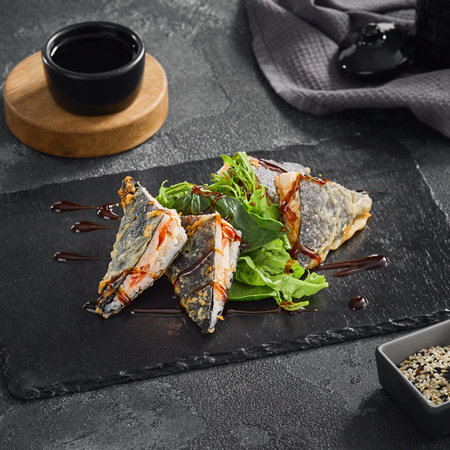 Crispy tempura onigiri sushi sandwich drizzled with rich unagi sauce, elegantly presented on a black stone plate.の写真素材