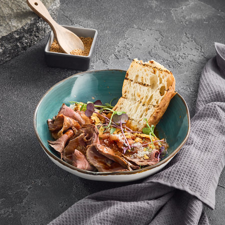 Succulent slices of roast beef served with toasted ciabatta bread in a teal ceramic bowl, garnished with sprouts.の写真素材