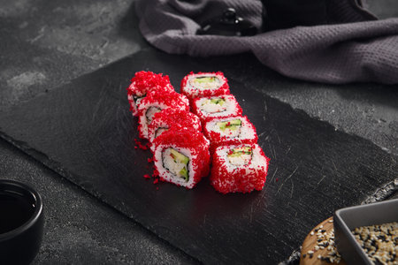 Vibrant California roll filled with crab and avocado, topped with bright red tobiko, served on a sleek black slate.の写真素材