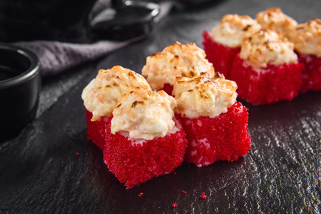 Succulent baked California roll topped with creamy crab, coated in a crispy tobiko crust, served on an elegant black slate.の写真素材