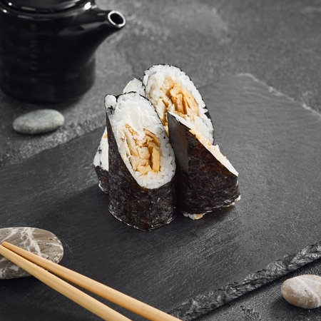 Traditional hosomaki sushi with savory eel and sweet tamago omelet, neatly presented on a black slate board.の写真素材