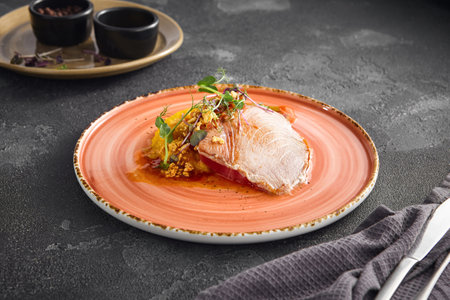 Seared tuna steak with a side of vibrant sweet potato puree, artistically plated on a ceramic dish with a black textured background.の写真素材