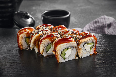 A delectable Canada maki roll with succulent eel and rich unagi sauce, sprinkled with sesame seeds, presented on a black slate.の写真素材