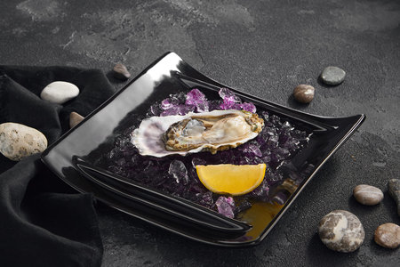 Exquisite Hassanakaya oyster, chilled on ice with a fresh lemon slice, presented on a chic black...