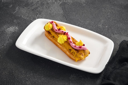 Vibrant raspberry Ã©clair with passion fruit glaze and decorative cream swirls on a rectangular...