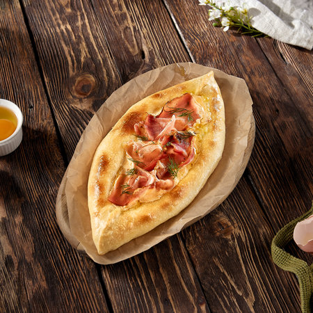 Adjarian khachapuri with bacon, garnished with dill on a rustic wooden table, invoking traditional Georgian flavors.の写真素材
