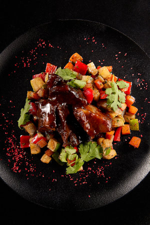 Braised beef cheeks with a vibrant vegetable ratatouille, served on a rustic black plate, autumn harvest-inspired.の写真素材
