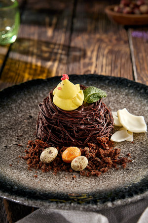 Nest-shaped pastry with a chick, served on a speckled plate.