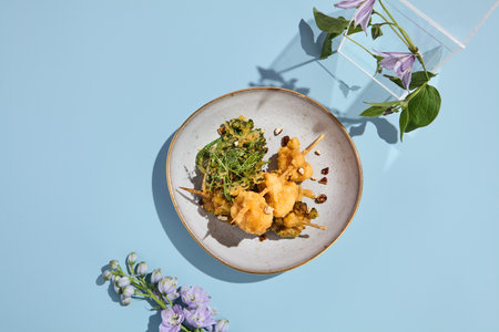 Elegant tempura vegetables on skewers with nut sauce amidst a surreal pastel floral backdrop.の写真素材