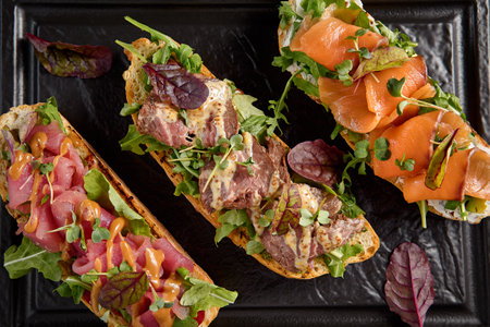 Top view of a bruschetta set with salmon, roast beef, and tuna on a textured black plate.の写真素材