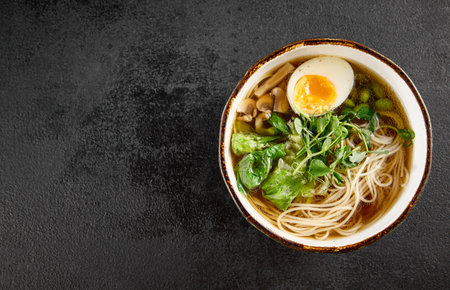 Aromatic ramen with a soft-boiled egg, leafy greens, and mushrooms, served in a rustic blue bowl.の写真素材