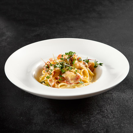 Classic carbonara pasta with a creamy sauce and garnished with fresh herbs, presented on a white plate.の写真素材