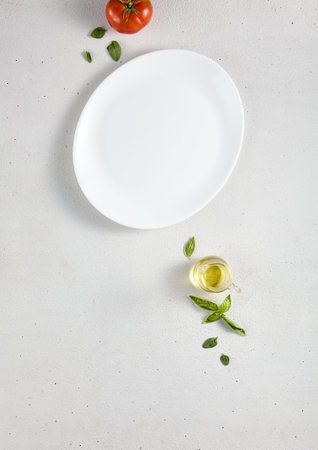 Elegant empty plate with basil leaves and olive oil on a textured background, top view. Perfect for...