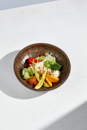 Salad bowl with avocado, mixed vegetables, and poached egg in bright sunlight.の写真素材