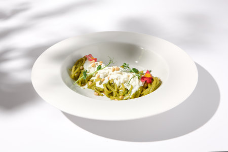 Spaghetti with Pesto Sauce and Stracciatella Cheese, Shadow of a Leaf on White, Ideal for Seasonal Menu Features.の写真素材