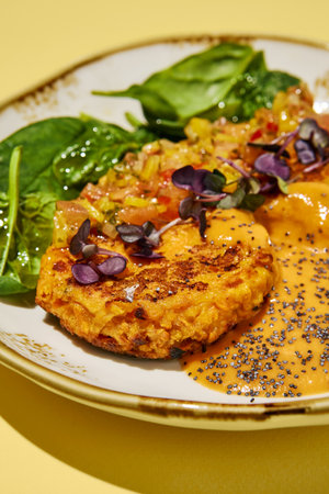 Close-Up of Vegan Sweet Potato Cakes with Vegetable Salsa and Spinach on a Yellow Background. Ideal for Healthy Lifestyle and Plant-Based Diet Promotions.の写真素材