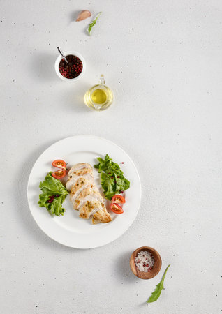 Grilled chicken breast with fresh lettuce and cherry tomatoes on white plate, ideal for healthy eating and diet concepts.の写真素材