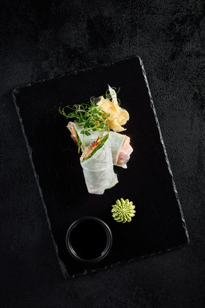 Top view of a salmon and avocado sprint roll with green pea sprouts on a textured black slate.の写真素材