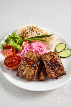 Barbecue pork ribs with fresh vegetable garnish and flatbread, perfect for grill menus and culinary blogs.の写真素材