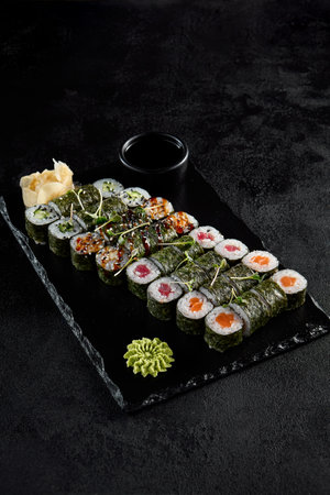 Assorted hosomaki sushi set with salmon, tuna, eel, and cucumber on black textured background.の写真素材