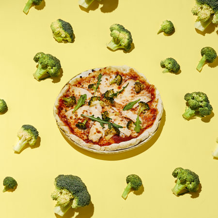 Top view, flat lay of a healthy gluten-free pizza with turkey and broccoli, surrounded by fresh broccoli on a yellow background.の写真素材