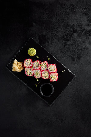 Top view of a California roll with tobiko and crab on a black slate board with soy sauce, wasabi, and ginger.の写真素材
