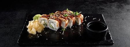 Canada roll with eel and unagi sauce, presented on a black slate with soy sauce and wasabi.の写真素材