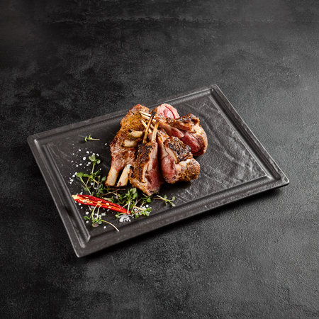 Perfectly grilled lamb rack served on a slate plate, with fresh herbs and a spicy red chili.の写真素材
