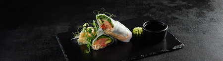 Salmon and avocado sprint roll with green pea sprouts on a black textured slate.の写真素材