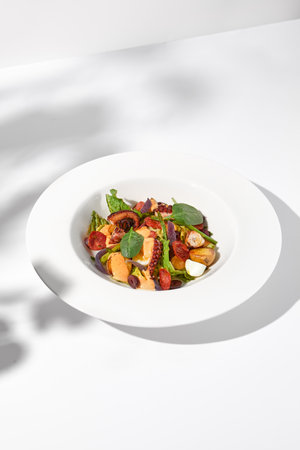 Mediterranean salad with octopus, potatoes, tomatoes, and Kalamata olives in a spicy sauce, shadowed on a white background.の写真素材