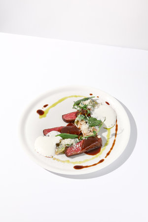 Pan-seared veal cutlet with cheese espuma and Demi-glace sauce on a sophisticated white plate for a refined culinary presentation.の写真素材
