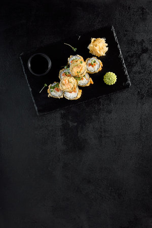 Salmon tempura roll top view on a textured black slate with condiments.の写真素材