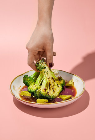 Woman's hand holding a broccoli steak in ponzu sauce, minimalist style.の写真素材