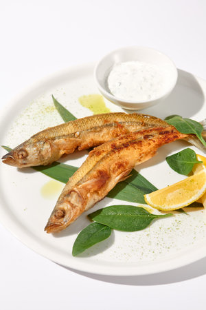 Grilled vendace fish with lemon and sour cream on a white plate, ideal for culinary presentations and food marketing.の写真素材