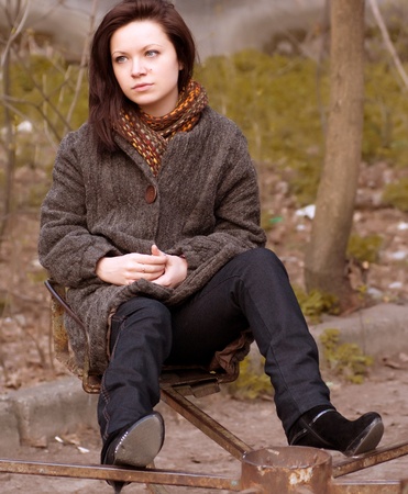 dreamy girl is sitting on a swing and looks into the distanceの写真素材