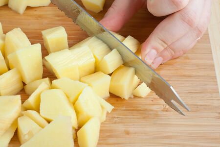 Female hands cutting potatoes on wooden board.の写真素材