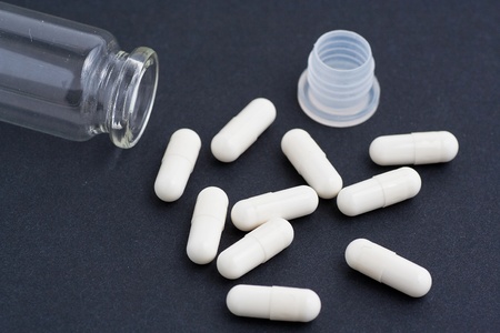 Large white pills spilling from a glass jar studio isolated against a black background.の写真素材