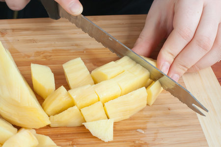 Female hands cutting potatoes on wooden board.