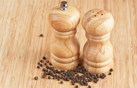 salt and pepper grinders on a table, with pepper spread aroundの写真素材