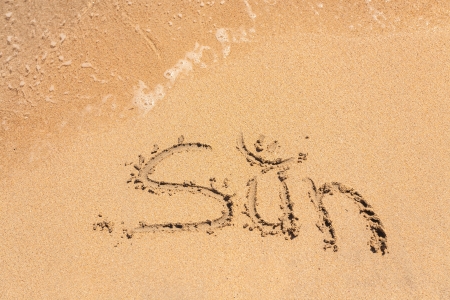 The Word Sun Written in the Sand on a Beach with Drawing of the Sun and Sea in Backgroundの写真素材