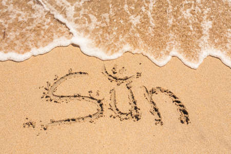The Word Sun Written in the Sand on a Beach with Drawing of the Sun and Sea in Backgroundの写真素材