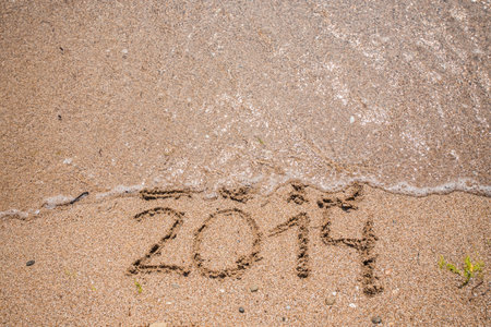 New Year 2014 is coming concept - inscription 2013 and 2014 on a beach sand, the wave is starting to...