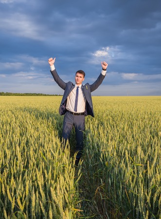 happy farmer, businessman, standing in wheat field over wind turbines with his hands up and thumbs upの写真素材